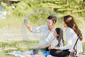 Happy family having fun outdoor sitting on picnic blanket taking selfie