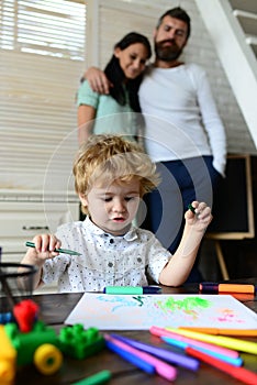 Happy family having fun, parents and little child painting writing in book with pencil making homework at home. Early