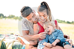 Happy family having fun together at picnic party - Joy and love concept with mother looking at father feeding child and playing