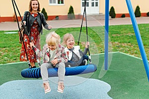 Happy family having fun together on playground. Happy childhood. Family vacation. Joyful little girls enjoying at modern swing.