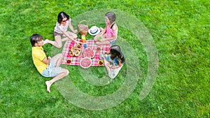 Happy family having picnic in park, parents with kids sitting on grass and eating healthy meals outdoors