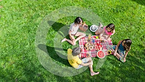 Happy family having picnic in park, parents with kids sitting on grass and eating healthy meals outdoors