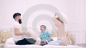 Happy family having pillow fight in bedroom. Mother, father and son laughing, playing and jumping in bed in bedroom at