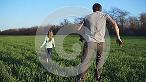 Happy family having a rest on a meadow on a sunny day. Father plays catch-up with his little daughter. Wide green field