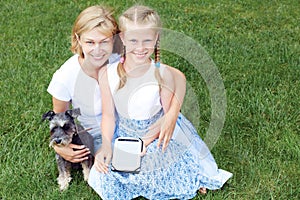 Happy family with his dog sitting on green grass and read e-book. Horizontal photo