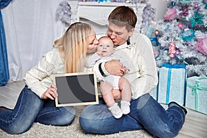 Happy family holding a blank Christmas card, sitting on the carpet in a cozy living room