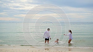 Happy family holding hands running along the shore. To run in the water creating splashes