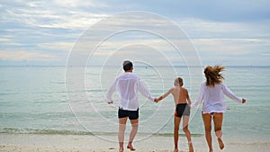 Happy family holding hands running along the shore. To run in the water creating splashes