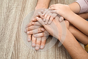 Happy family holding hands at wooden table, closeup