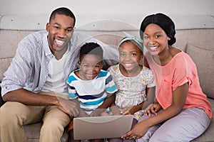 Happy family holding laptop while sitting on sofa at home