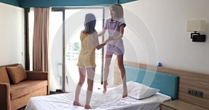 Happy family at home and children twin sisters jumping on bed playing and laughing