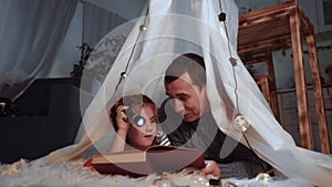 Happy family at home dream. Dad and daughter happy family at home reading a book in the evening in homemade wigwam house