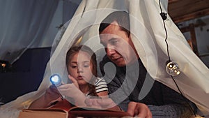 happy family at home dream. dad and daughter happy family at home reading a book in the evening in homemade wigwam house