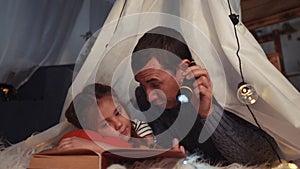 happy family at home dream. dad and daughter happy family at home reading a book in the evening in homemade wigwam stay