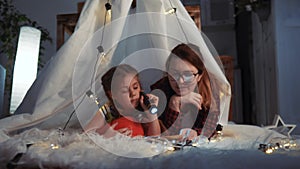 happy family at home dream. mom and daughter happy family at home reading a book in the evening in homemade wigwam house