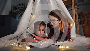 happy family at home dream. mom and daughter happy family at home reading a book in the evening in homemade wigwam house