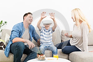 Happy family at home on living room sofa having fun playing games using virtual reality headset