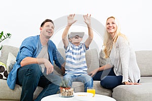 Happy family at home on living room sofa having fun playing games using virtual reality headset