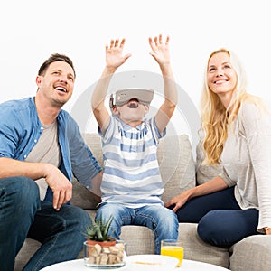 Happy family at home on living room sofa having fun playing games using virtual reality headset