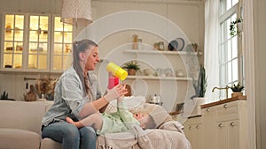 Happy family at home. Mother and baby girl playing in couch at home indoors. Little toddler child and babysitter nanny