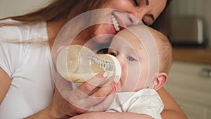 Happy family at home. Mother holding little baby toddler child feeding milk from bottle. Newborn Infant baby girl