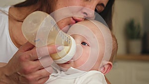 Happy family at home. Mother holding little baby toddler child feeding milk from bottle. Newborn Infant baby girl