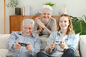 Happy family at home. Old senior man grandfather woman grandmother girl granddaughter playing video game with joysticks photo