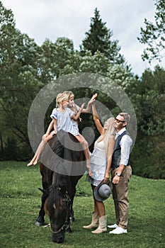 Happy family on the horse ranch walking with horse. Young happy family having fun at countryside outdoors, two girls