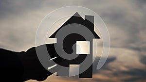 Happy family house lifestyle construction concept. Man holding home a paper house in his hands at sunset silhouette