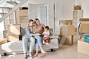 Happy family householders with kid sitting on couch at new home at moving day.