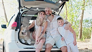 Happy family hugging while sitting in open trunk car with Akita Inu