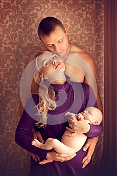 Happy family - husband, wife and newborn baby posing at home by