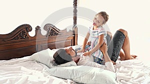 Happy Family Idyll Little Child Daughter Jump On Father Arms And They Fall On A Bed