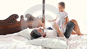 Happy Family Idyll Little Child Daughter Jump On Father Arms And They Fall On A Bed