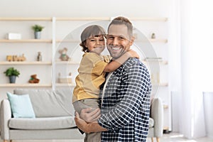 Happy family. Indoors portrait of positive caucasian man embracing his cute little son, holding him on hands