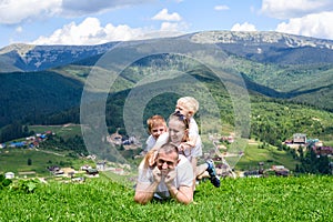 Happy family: joyful father, mother and two sons are lying on the green grass against the background of the forest, mountains and