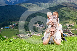 Happy family: joyful father, mother and two sons are lying on the green grass against the background of the forest, mountains and