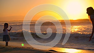 Happy family jump fun on the beach. Mom and daughter dance and play at sunset. Waves at dawn a child runs along the