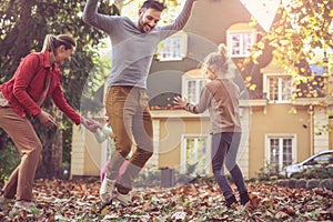 Happy family jumping at fall leaves at backyard.