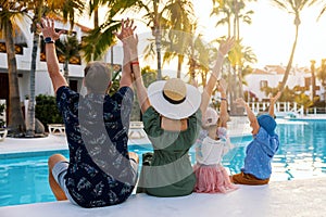 happy family with kids and arms raised having fun by the swimming pool at tropical resort hotel. summer vacation