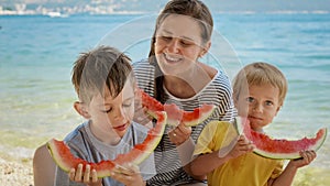 Happy family with kids eating watermelons on sandy sea beach during summer holiday vacation