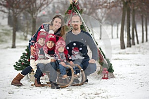 Happy family with kids, having fun outdoor in the snow on Christmas, playing with sledge