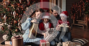 Happy family with kids sit near Christmas tree opening gifts