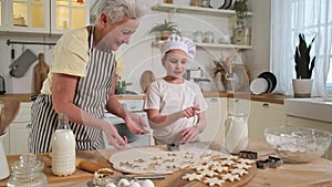 Happy family in kitchen. Grandmother granddaughter child cutting cookies of dough on kitchen table together. Grandma