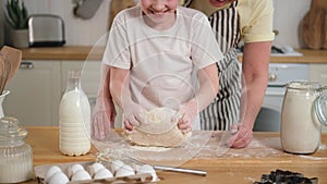 Happy family in kitchen. Grandmother granddaughter child hands knead dough on kitchen table together. Grandma teaching