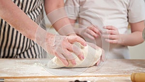 Happy family in kitchen. Grandmother granddaughter child hands knead dough on kitchen table together. Grandma teaching