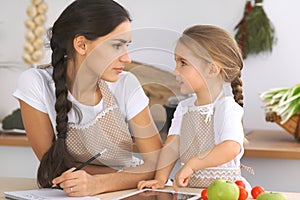 Happy family in the kitchen. Mother and child daughter make menue for cooking tasty breakfest in the kitchen. Little photo