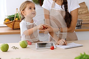 Happy family in the kitchen. Mother and child daughter make menue for cooking tasty breakfest in the kitchen. Little