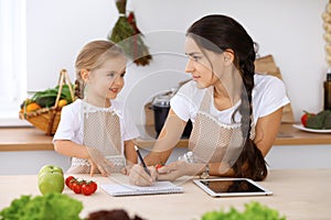 Happy family in the kitchen. Mother and child daughter make menue for cooking tasty breakfest in the kitchen. Little