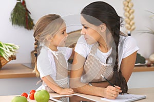 Happy family in the kitchen. Mother and child daughter make menue for cooking tasty breakfest in the kitchen. Little photo